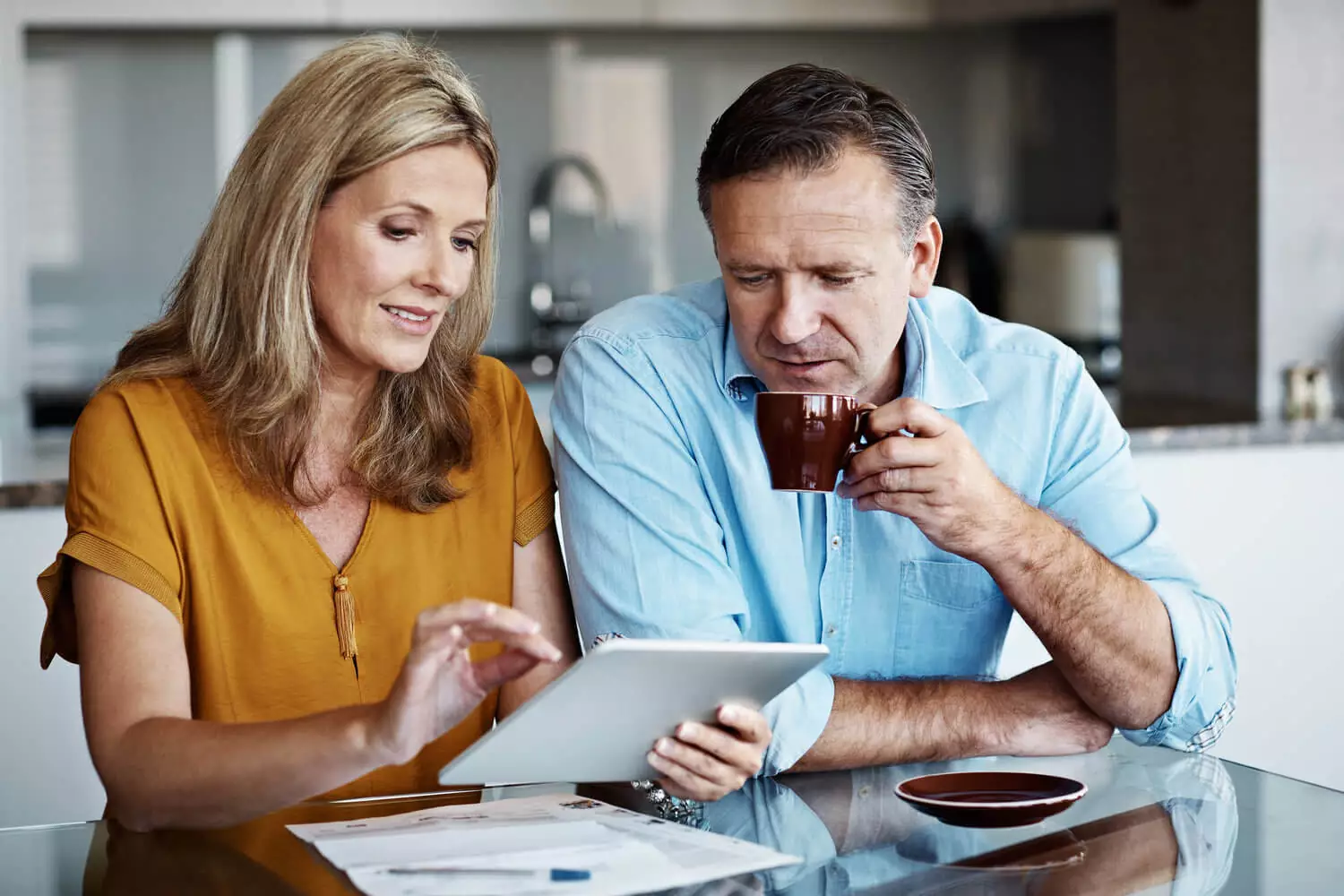 Couple talking to each other with the woman holding her tablet device and the man drinking his coffe