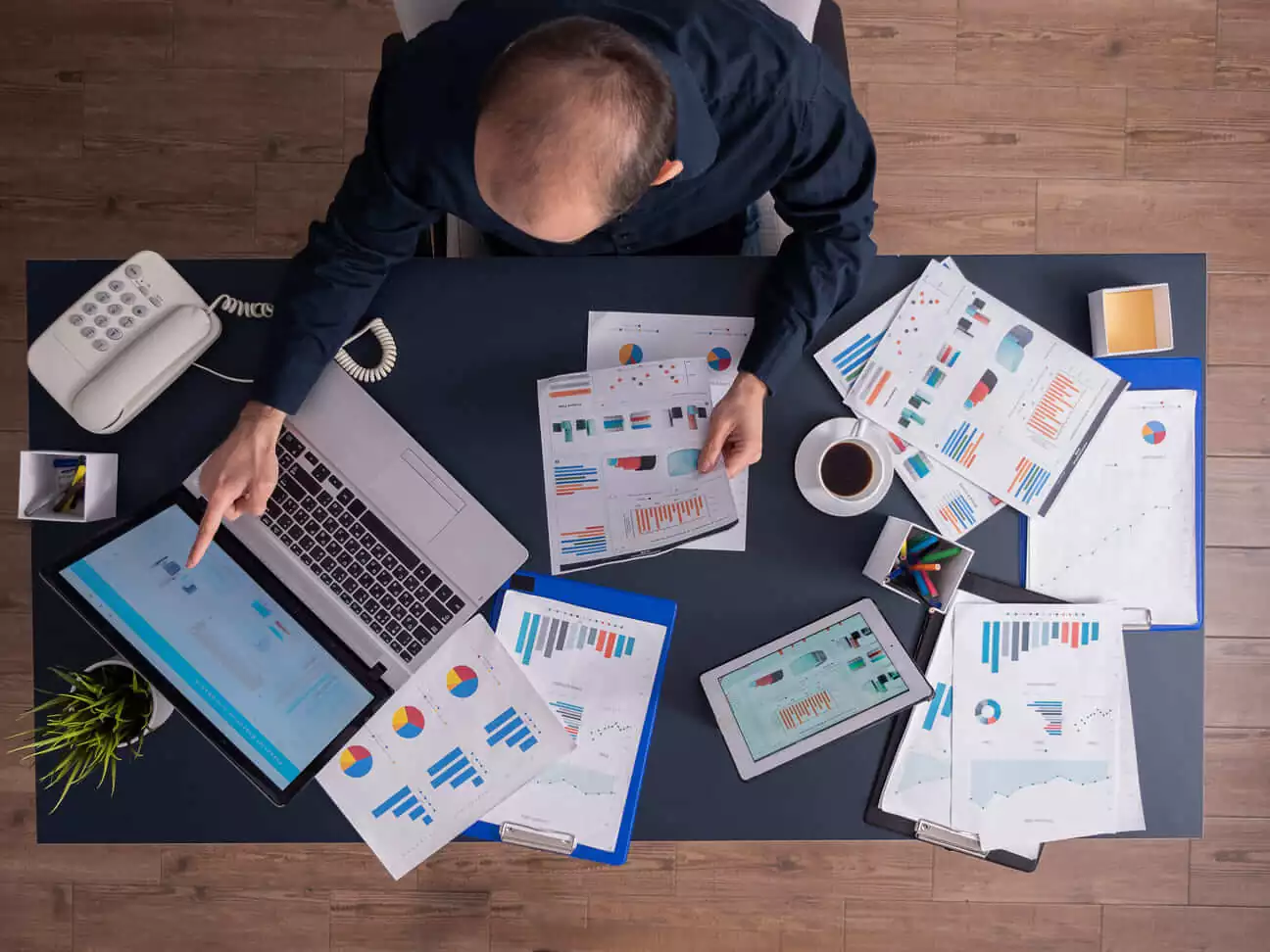 Top view of a man pointing on his laptop with bar and pie graphs